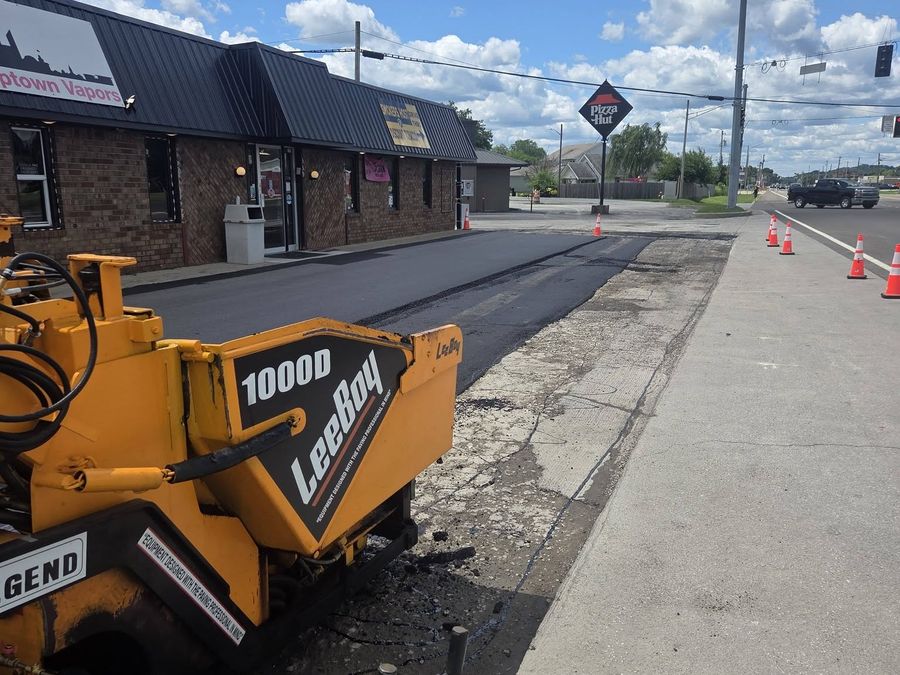 Asphalt paver laying a fresh mat along a commercial lot