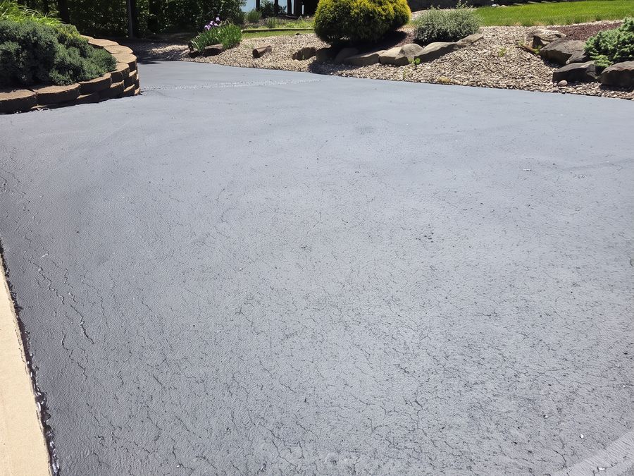Finished black asphalt driveway with landscaping in front of a brick home